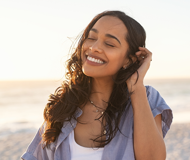 Woman with wavy hair smiling at beach during sunset